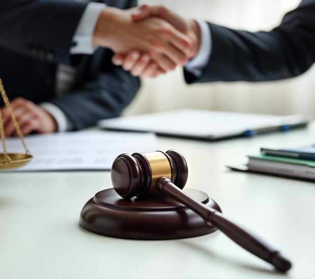 Gavel on a table with two people shaking hands.