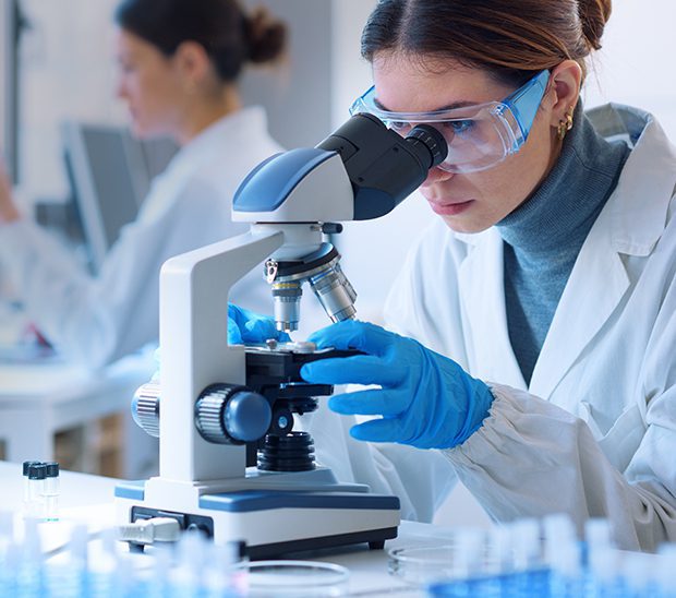 Scientist observing samples through a microscope in a lab.