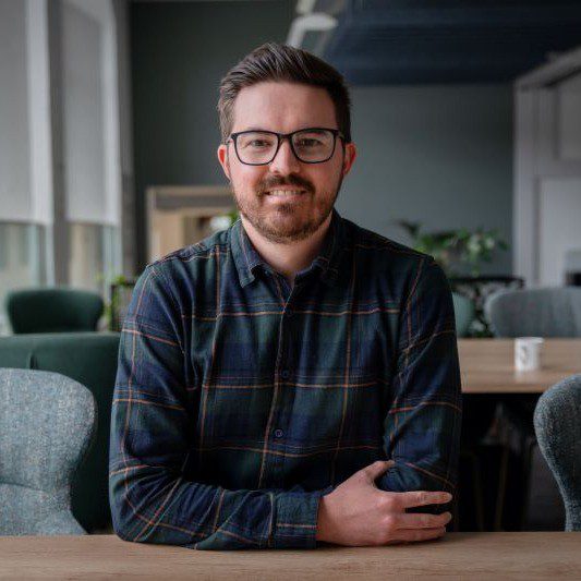 Young man with glasses smiling at a desk.