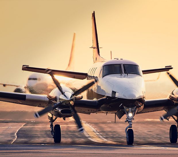 A twin-engine aircraft is on a runway at sunset, with warm light illuminating its front.