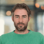 Man with a beard wearing a green sweater, smiling.