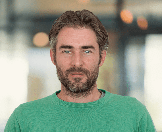 Man with a beard wearing a green sweater, smiling.