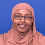 Smiling woman wearing glasses and a brown hijab.