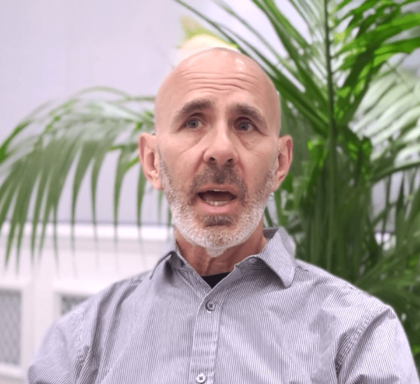 Man speaking with a serious expression, surrounded by plants.