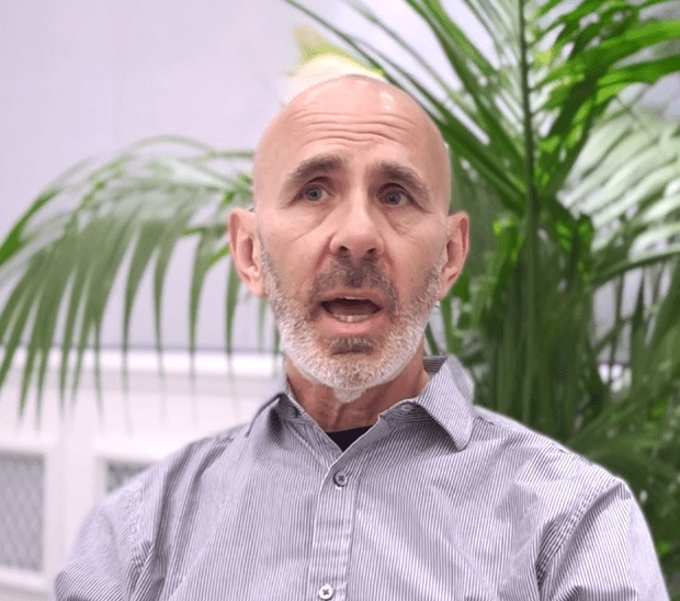 Man speaking with a serious expression, surrounded by plants.