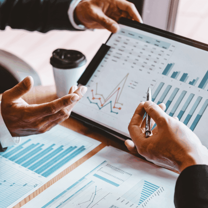 Hands discussing data on a tablet and documents.