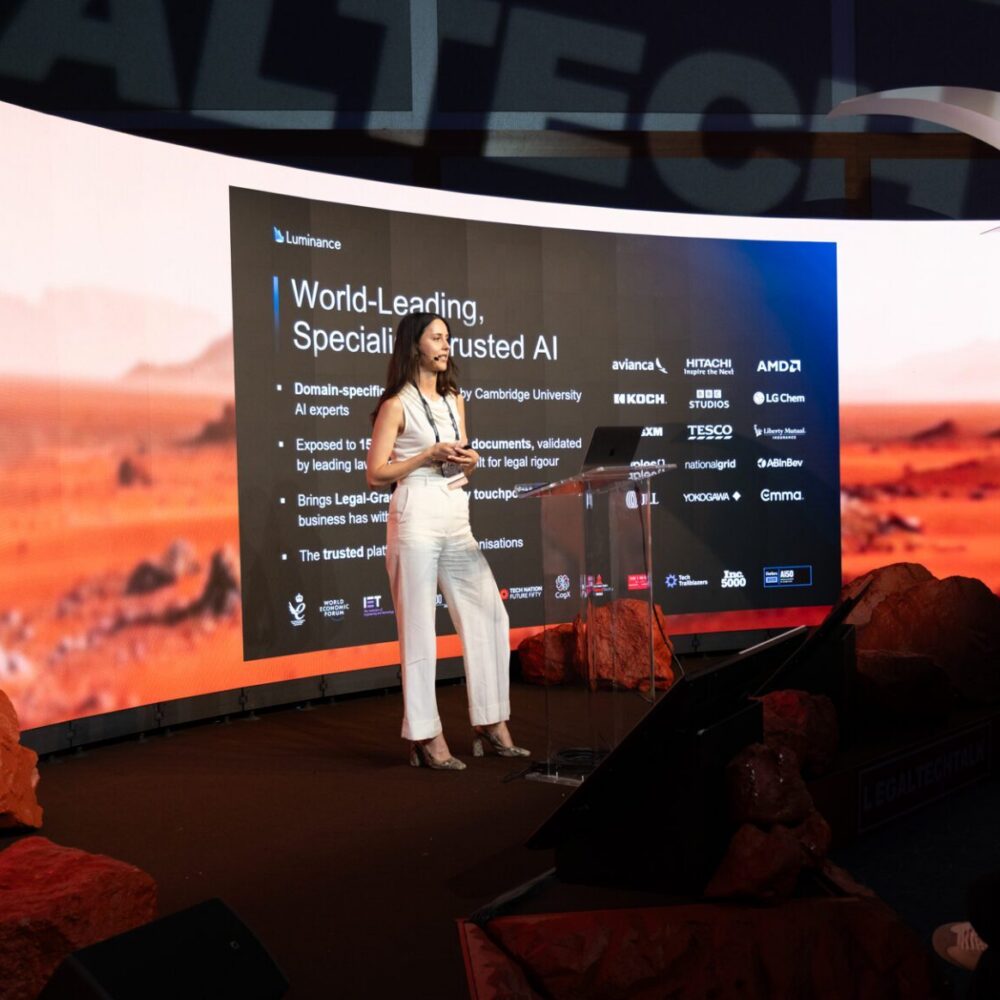 Presenter speaking at a technology event with a digital display.