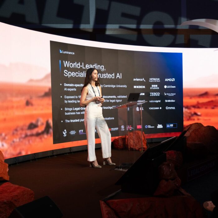 Presenter speaking at a technology event with a digital display.