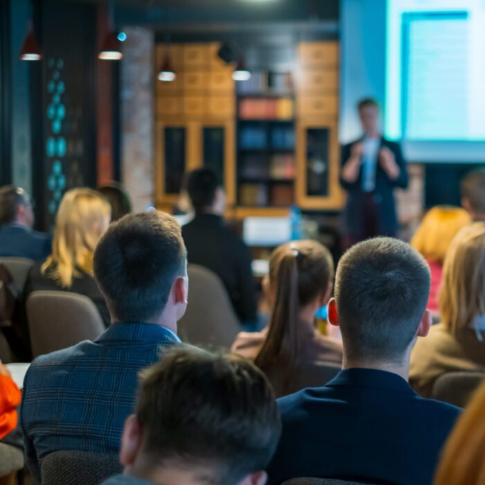Audience listens lecturer at workshop in conference hall, rear view
